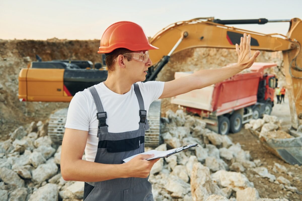 Management of project. Worker in professional uniform is on the borrow pit at daytime